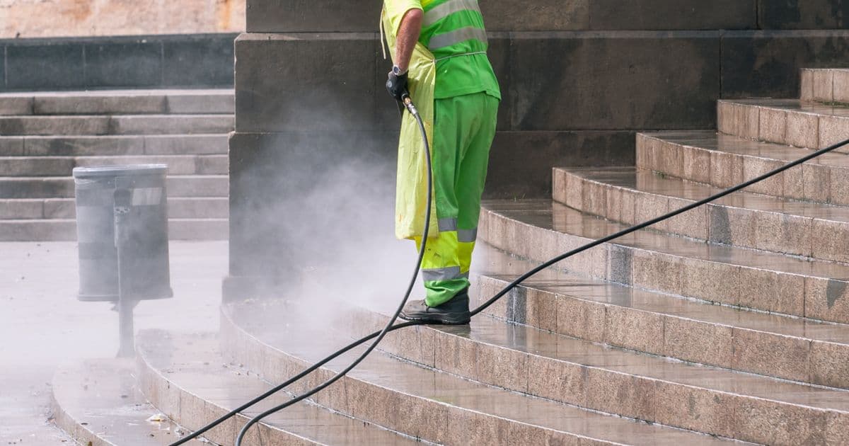 A pressure washing operator in hi-vis gear cleaning stone stairs on a job site