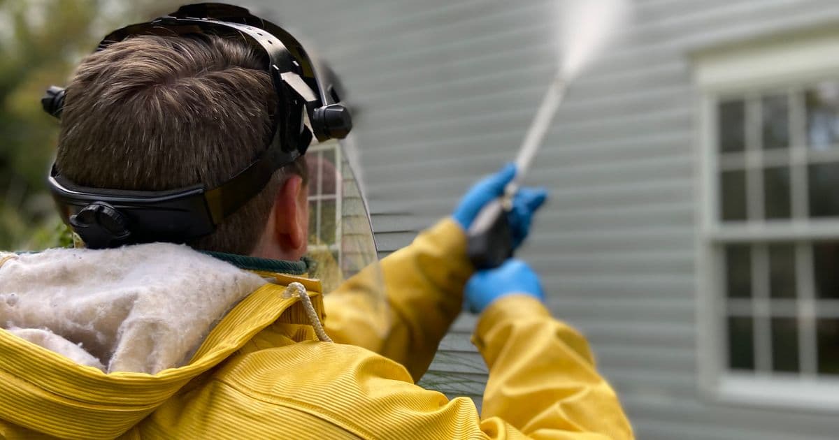 Operator pressure washing the exterior siding of a residential house — vinyl siding soft wash in progress